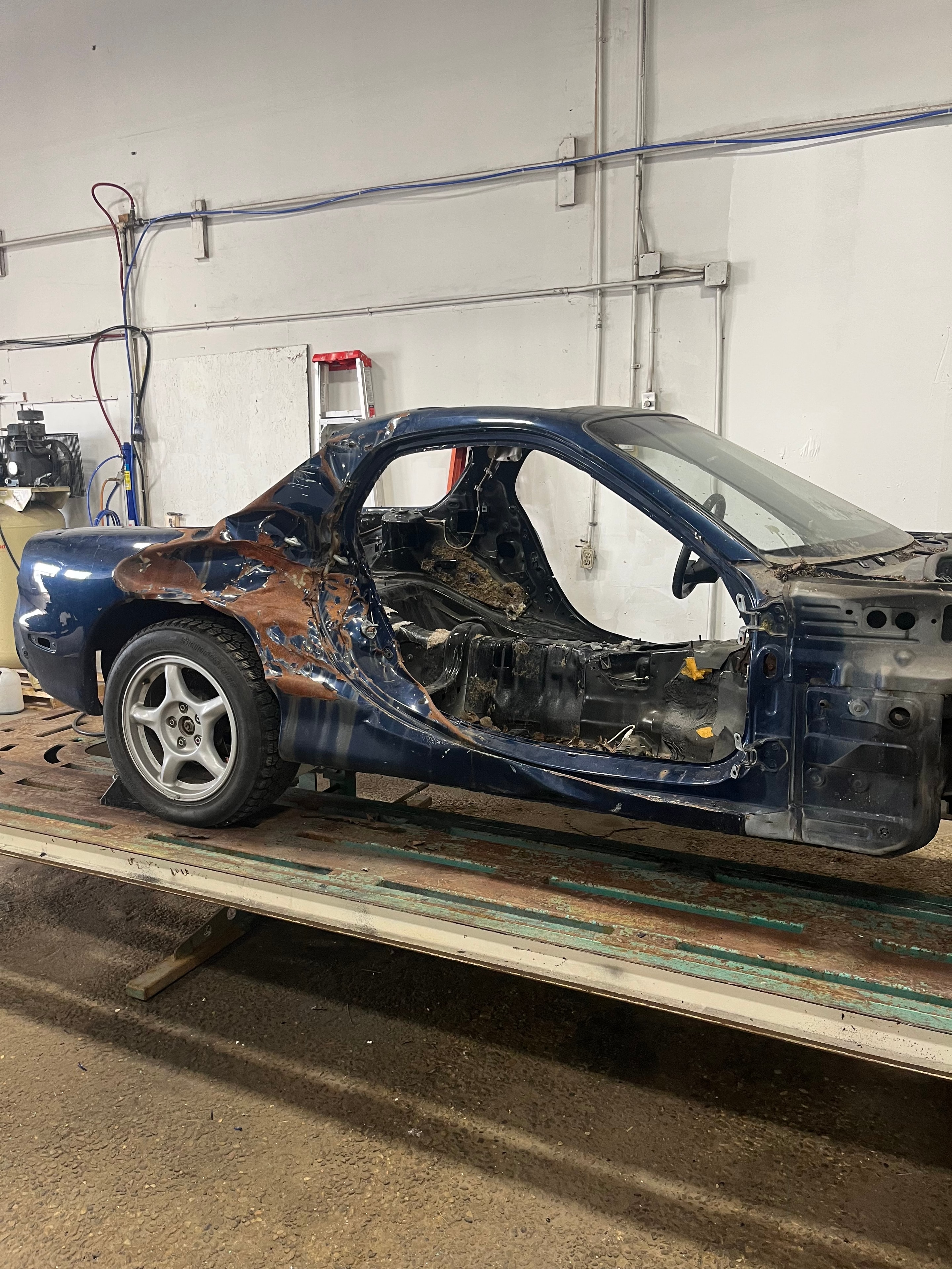 Damaged blue vehicle body before frame correction in the MACART workshop